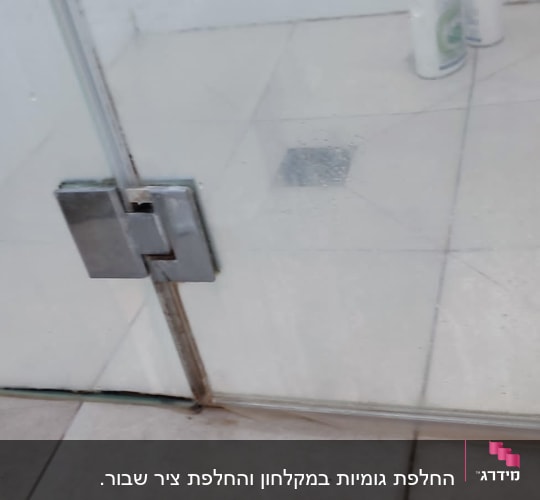 דלת זכוכית למקלחת עם בקבוקי שמפו על הרצפה